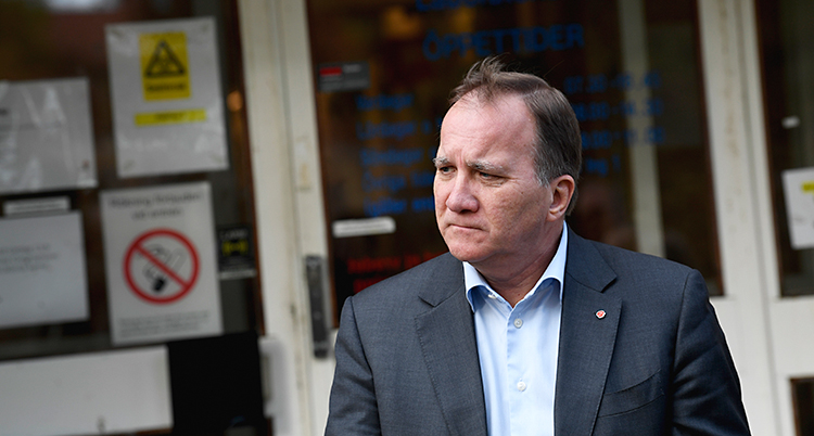 En bild på statsminister Stefan Löfven. Han är utomhus och står framför ett hus. Han har en kavaj och en skjorta. Han tittar åt sidan.