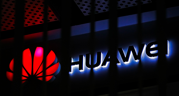 Bilden visar en skylt för företaget Huawei. Skylten lyser i mörkret. Det är en röd symbol och bredvid symbolen står det Huawei.