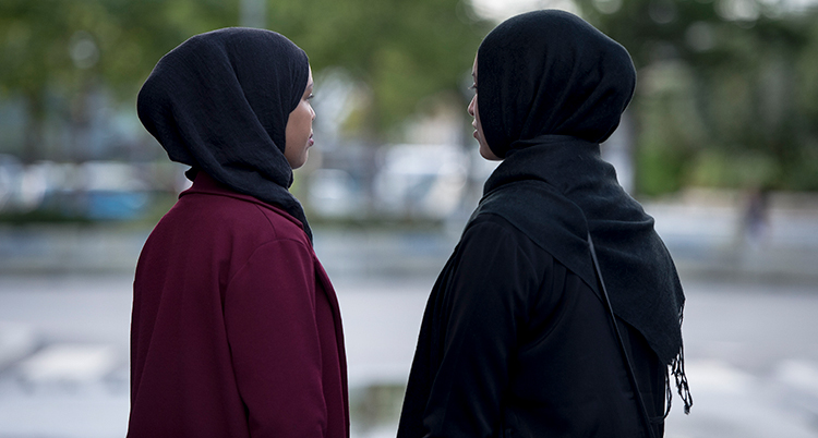 Två kvinnor med svarta sjalar runt håret står med ryggen mot kameran.