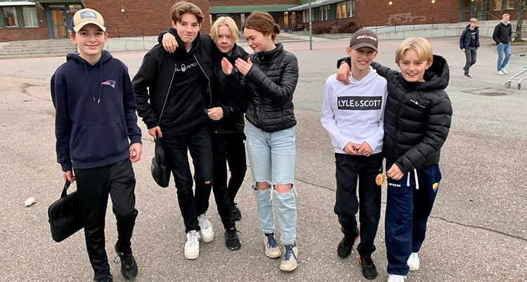 Ett gäng med ungdomar. går över en skolgård. De ser glada ut och håller om varandra.