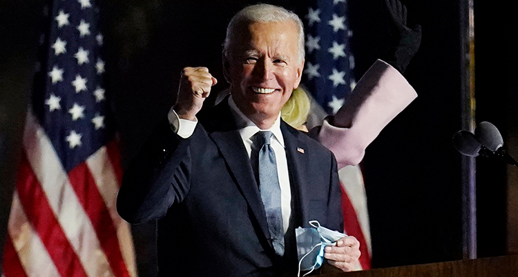 Biden ler och håller upp en näve i luften. Amerikanska flaggor är bakom honom.