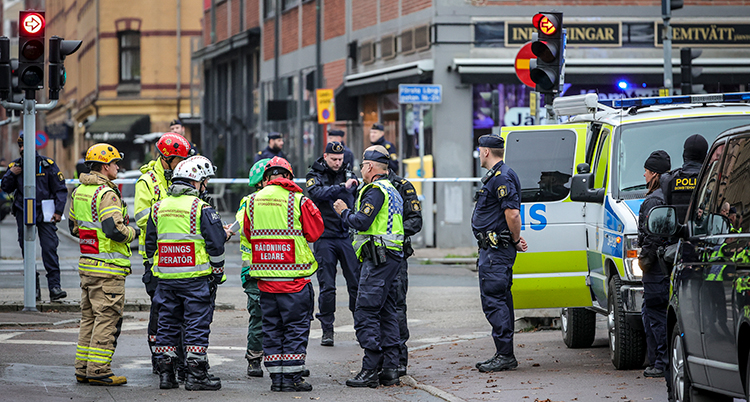 Brandmän och poliser står vid en polisbil.