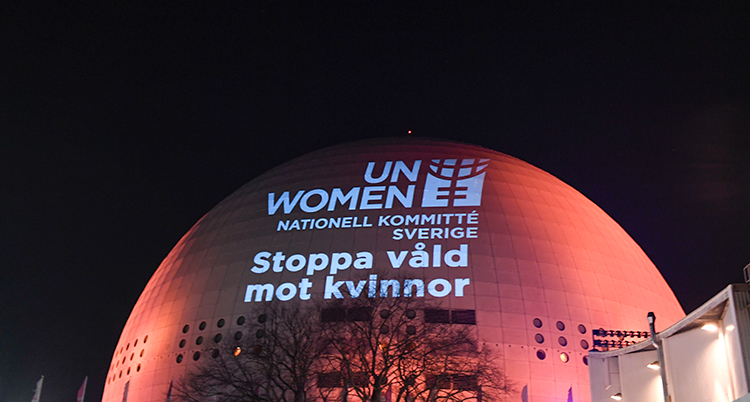 Globen upplyst i orange mot en svart himmel. I vitt lyser texten Stoppa våld mot kvinnor på Globen.