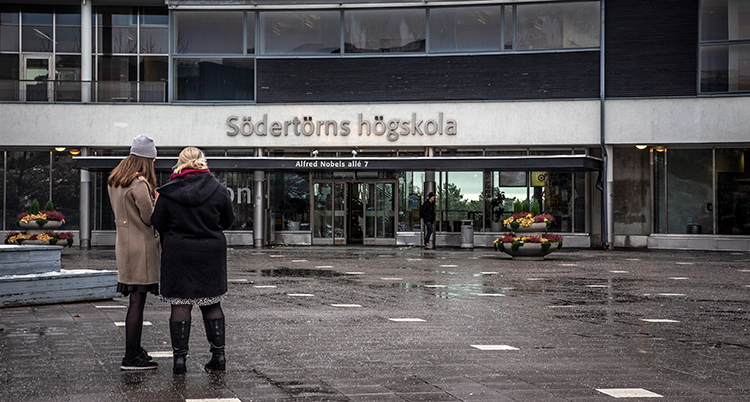 Två kvinnor, iklädda jackor och med ryggarna mot kameran, står utanför entrén till Södertörns högskola