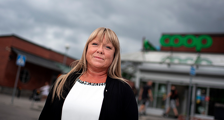 En kvinna med långt ljust hår, vit tröja och svart kavaj står framför en Coop-butik