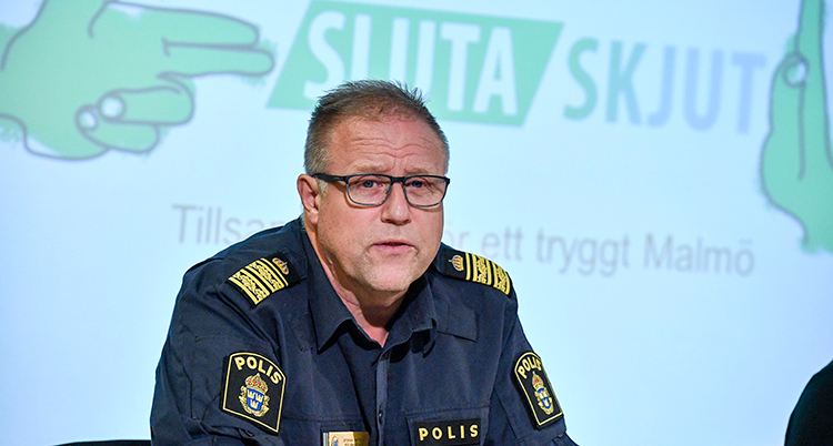 Han talar i en mikrofon. Bakom honom står det Sluta skjut på en skärm.