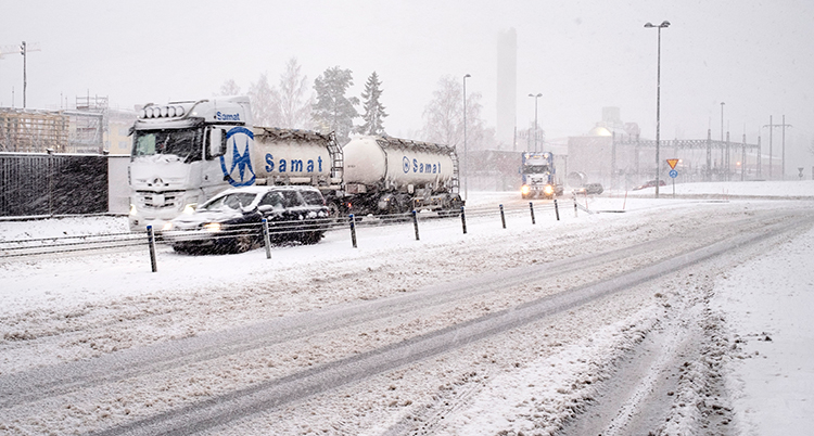 Bilar och en stor lastbil åker på en väg med massor av snö.