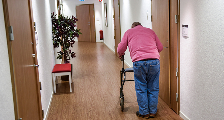 en äldre man går med rollator i en korridor.
