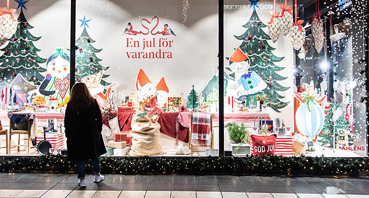 En person står utanför en affär. I affärens fönster finns tomtar och julgran och annat.