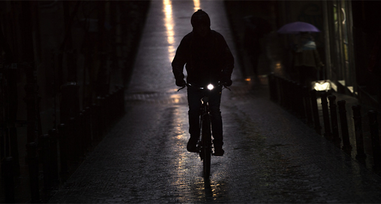 Det är mörkt ute. En person kommer cyklande mot kameran. Det är ett lyse tänt på cykeln.