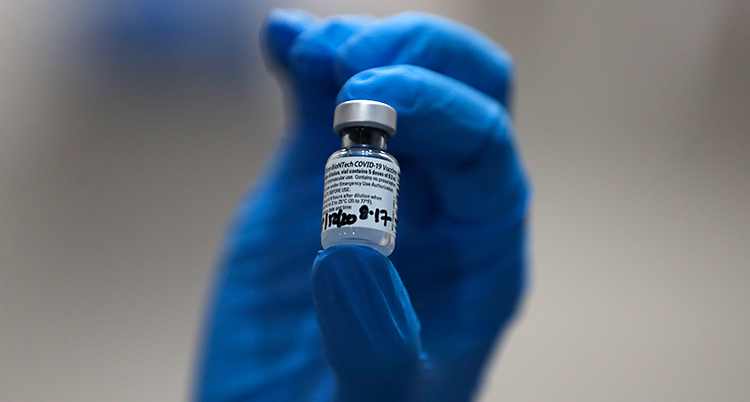 En närbild på en liten glasburk med lock. Det är vaccin i burken. En hand med en blå handske håller i burken.