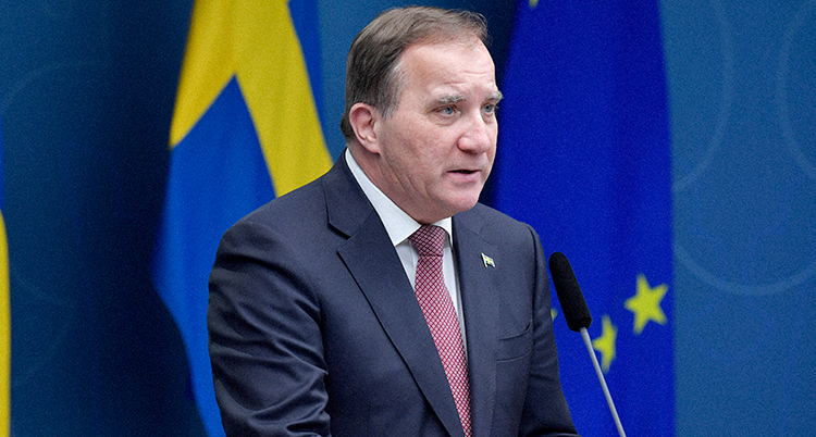 Löfven ser allvarlig ut. Han pratar i en mikrofon som står framför honom. Bakom honom är en svenska flagga.
