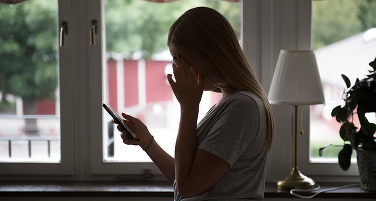 En siluhett av en kvinna som håller i en mobil med ena handen och tar sig i ansiktet med den andra.