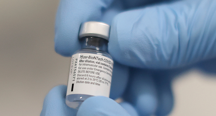 Två händer med plasthandskar håller i en liten flaska med vaccin.