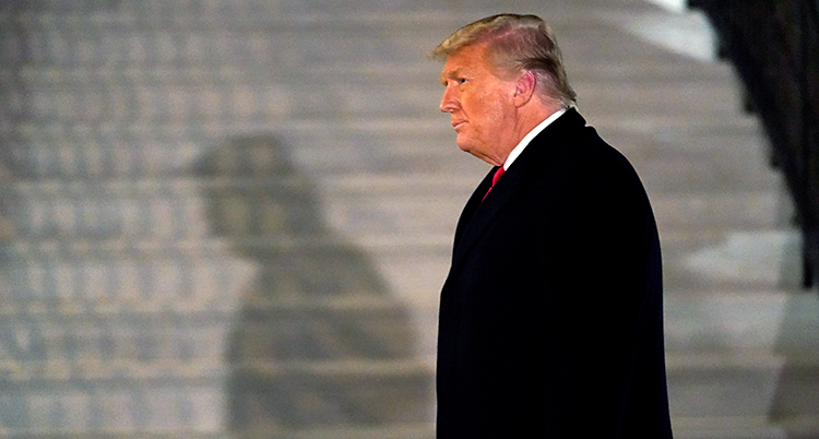 Donald Trump går utanför Vita huset. Vi ser honom i profil. Han har en svart rock på sig.