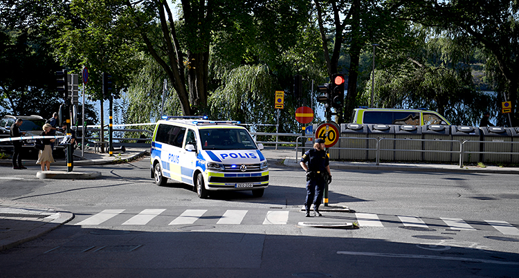 En gata i Stockholm. Poliser har spärrat av med vita och blå band. Vi ser en polisbil och poliser som går på gatan.
