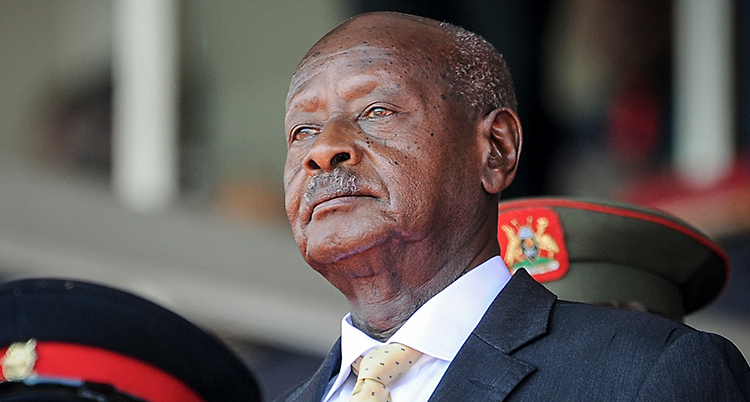 En närbild på presidenten i Uganda som heter Yoweri Museveni. Han är en äldre man med snaggat huvud och en mustasch. Han har kostym. Bredvid honom står några militärer.