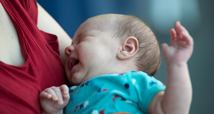 En baby I blå tröja ligger i en kvinnas famn