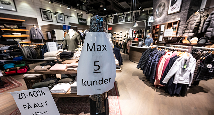 En butik med hyllor och rack med kläder. En skylt säger att bara fem får vara i butiken. Butiken är tom på människor.