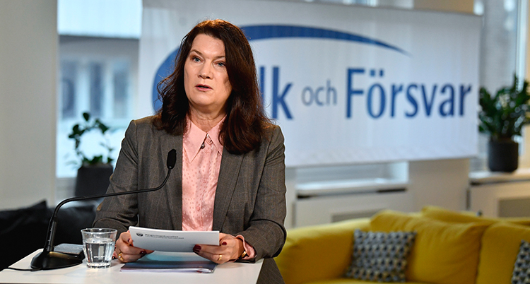 Hon står vid ett bord och talar. Bakom syns en skylt med texten Folk och Försvar.
