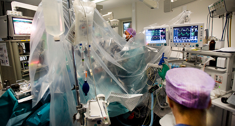 En patient ligger bakom ett skynke. Skärmar syns i rummet.
