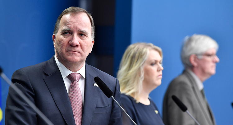 Statsministern tittar framåt, bakom honom syns Lena Hallengren och Johan Carlsson. De är klädda i kostymer och dräkt.