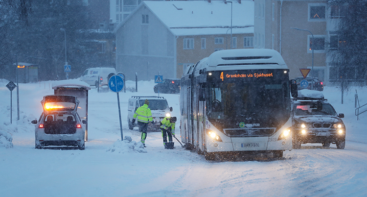 Två personer skottar snö runt bussens däck.
