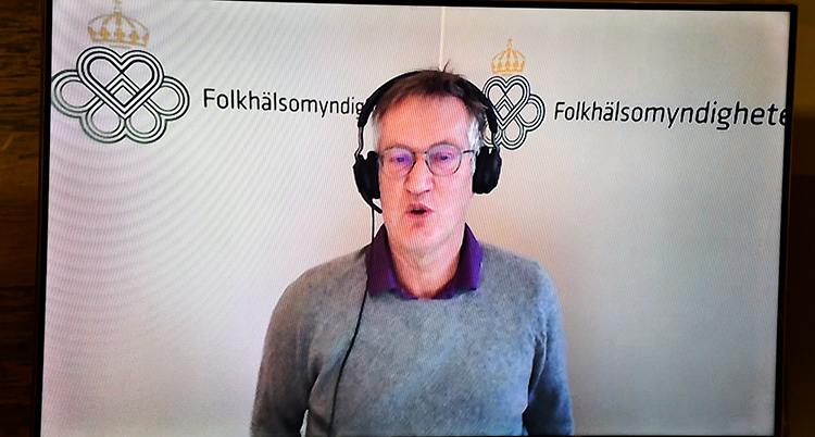 En filmad bild när han står och berättar. Han har hörlurar med en mikrofon på sig.
