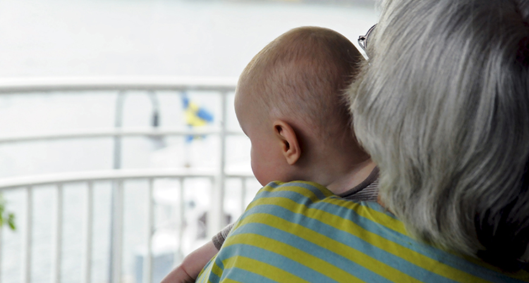 En gammal kvinna håller i en liten bebis. Deras ansikten syns inte.