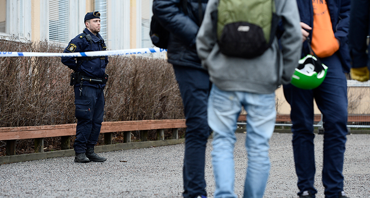 En polis stor bakom ett band där det står polis. Det har hänt ett brott och han vaktar. Några unga står på andra sidan bendet. Man ser deras ryggar