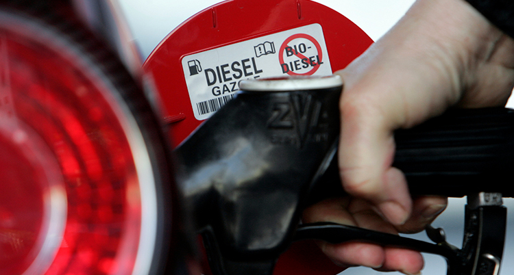 En hand håller i ett munstycke och tankar diesel i tanken på en bil.