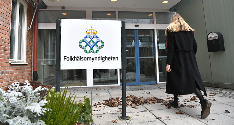 En kvinna är på väg mot en glasdörr. Man ser bara ryggen och hennes långa ljusa hår. Bredvid henne är en skylt där det står Folkhälsomyndigheten.