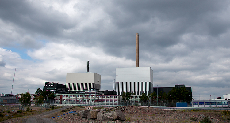 En bild på långt håll av kärnkraftverket. Mörka moln är på himlen.