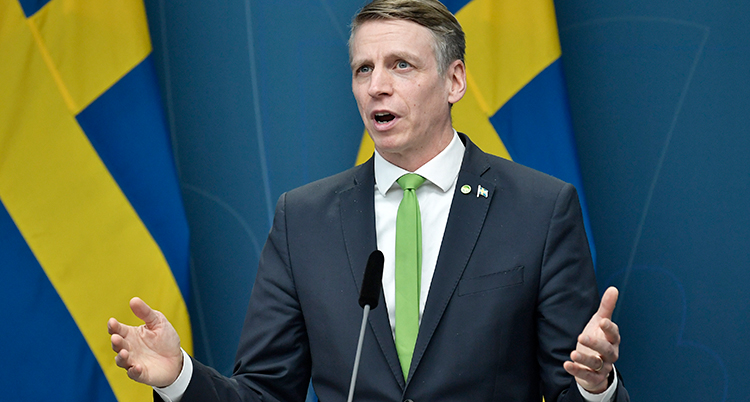 Han slår ut med händerna när han pratar. Bakom honom syns Svergies flagga.