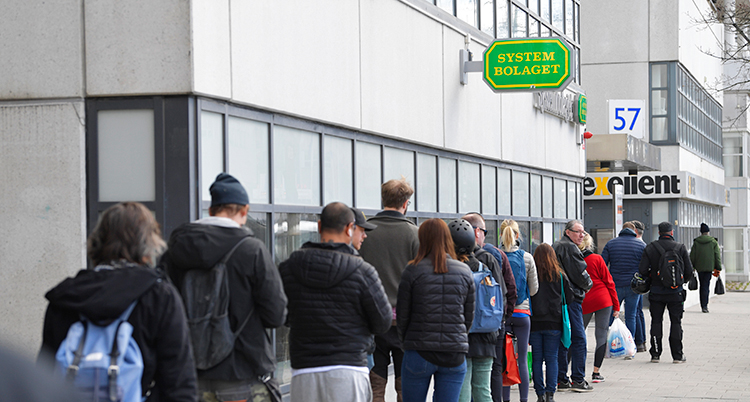 Människor står i en kö på trottoaren utanför Systembolaget