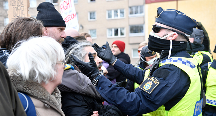 poliser med munskydd framför människor som trängs.