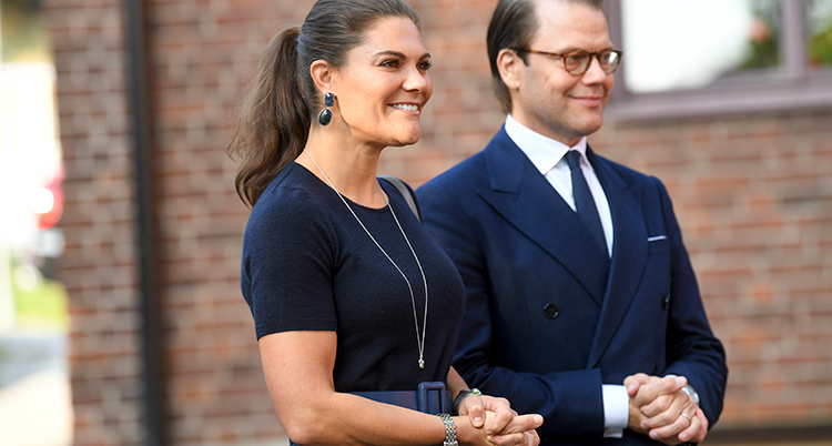 Victoria och Daniel ler och står med knäppta händer och tittar på något.