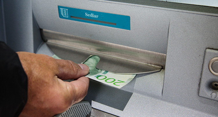 En hand tar emot en sedel som det står 200 kronor. Sedeln kommer ut ur en lucka.