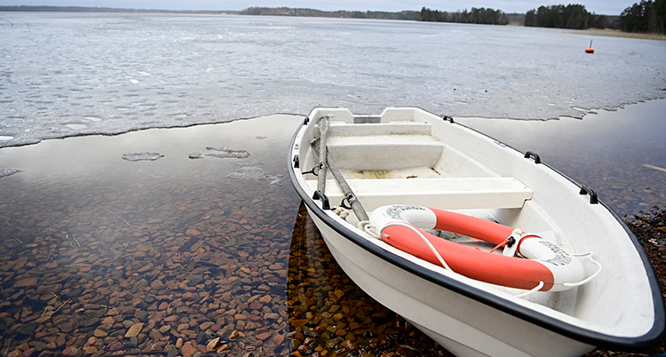 En båt ligger på en strand. I den ligger en livboj. Bakom en sjö med is. Men vid kanten syns det att isen är mycket tunn.