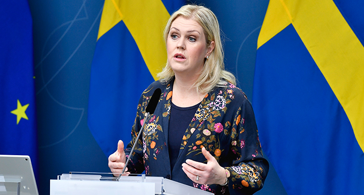Hallengren står en talarstol.Hon har en kavaj med blommor. Hon talar och ser allvarlig ut.