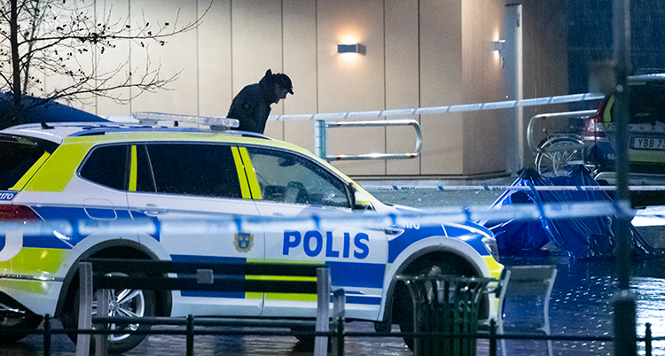 En polisbil syns. Det är mörkt. En polisman syns bakom bilen.