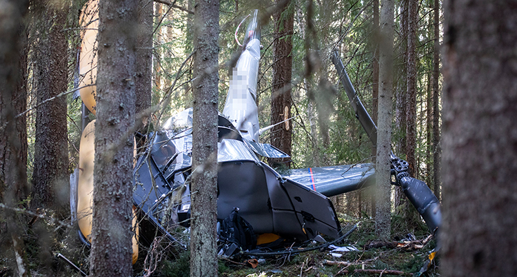 En helikopter ligger på marken i skogen. Den är helt förstörd.
