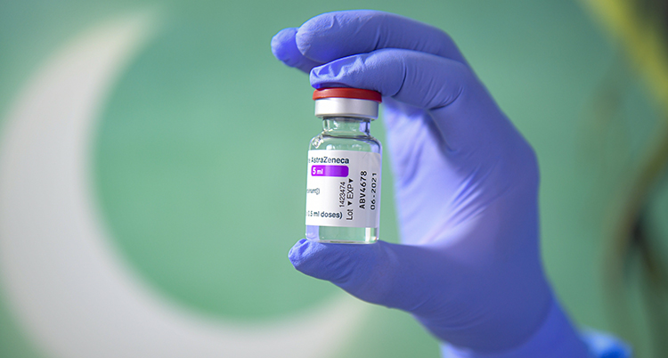 En hand med blå plasthandske håller i en liten flaska med vaccin.