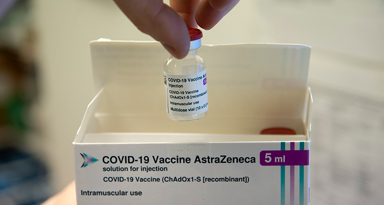 En hand håller en lite flaska vaccin över en kartong.