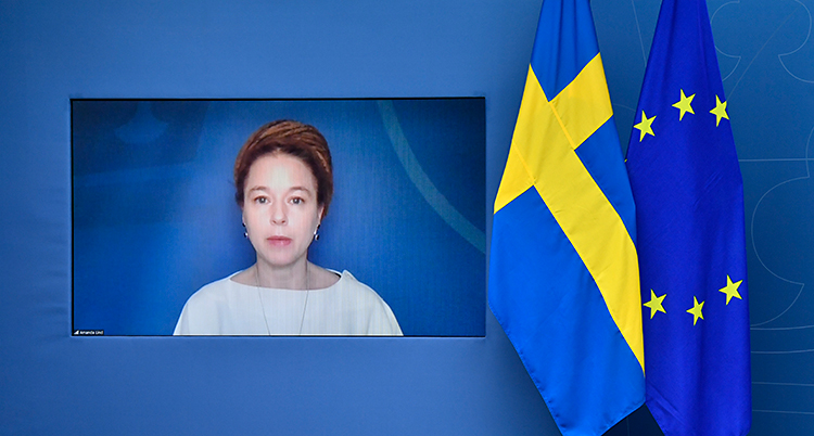 Amanda Lind pratar på en stor videoskärm. Bredvid skärmen finns en svensk flagga och EUs flagga.