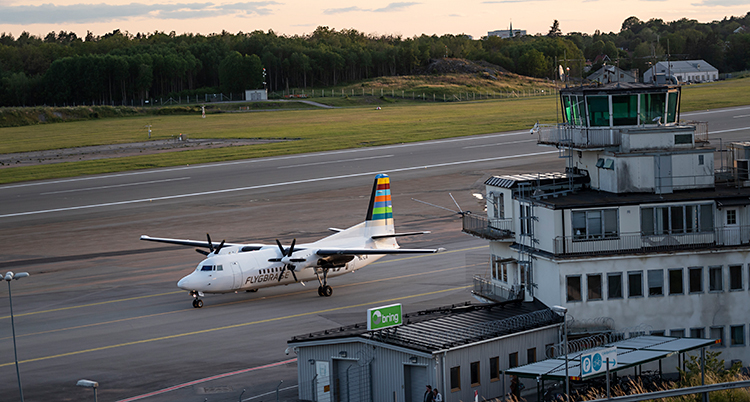 En bild från Bromma flygplats. Vi ser byggnaden. I bakgrund finns en bana. Där står ett flygplan.