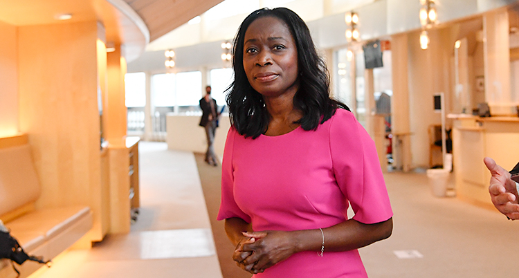 Nyamko Sabuni står i riksdagens hus. Hon tittar mot kameran. Hon har på sig en rosa klänning.