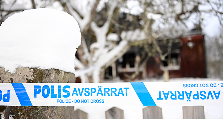 En bild från februari. Det är snö ute. Poliserna har satt upp band vid ett staket. I bakgrunden syns ett hus som är skadat av en brand.