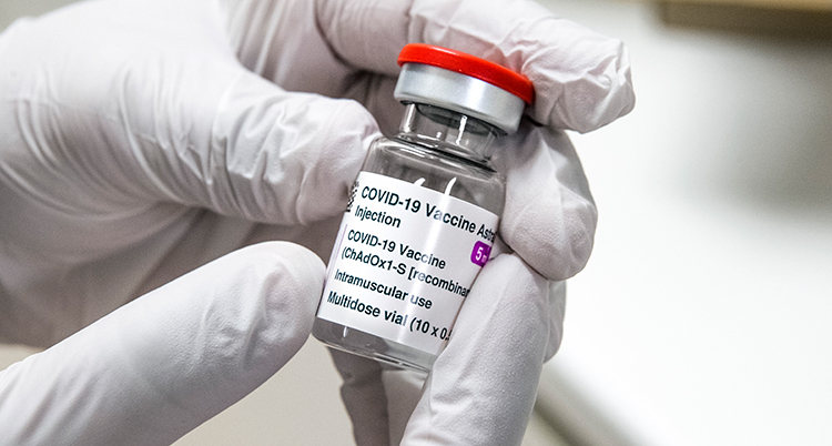 Två händer med plasthandskar håller i en liten flaska med vaccin.