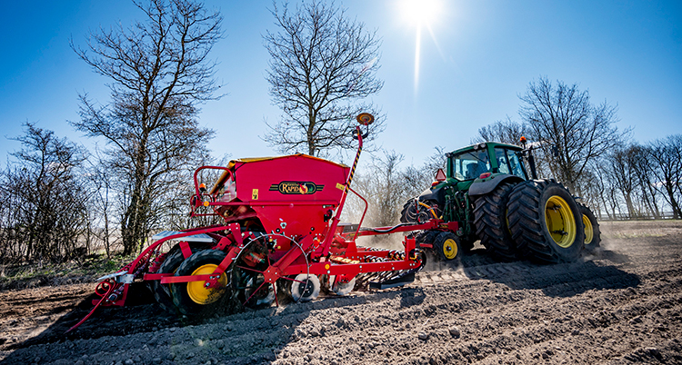 En röd spridare efter en traktor på en åker